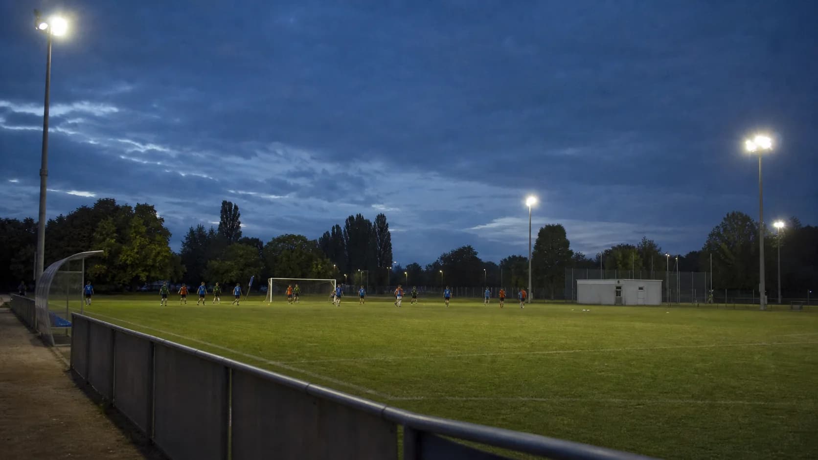 Real football pitch during training from a touchline or player-level viewpoint, showing all mast positions and believable uniformity; no fictional crowd.