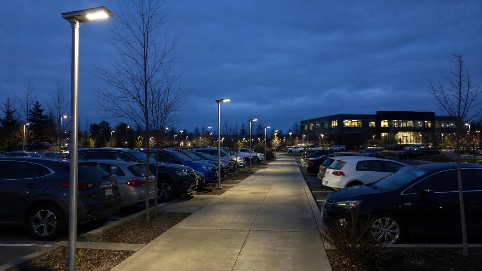 Real parking or service area with solar poles, bays, pedestrian route, landscape shading and open sky visible; avoid perfectly empty architectural stock imagery.