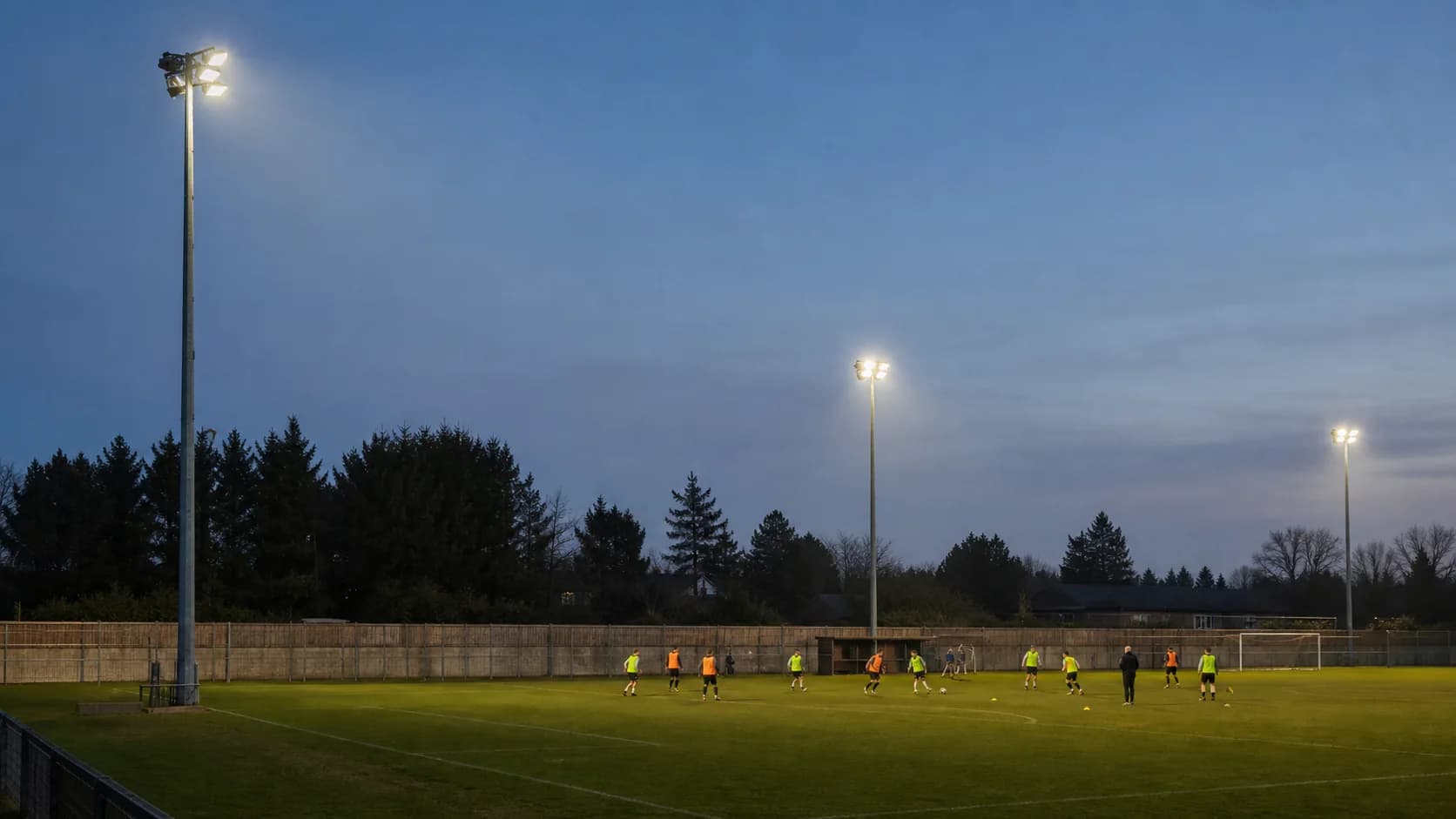 Real evening sports field from a player-level viewpoint, showing mast locations and even playing-surface coverage; avoid a packed fictional stadium.